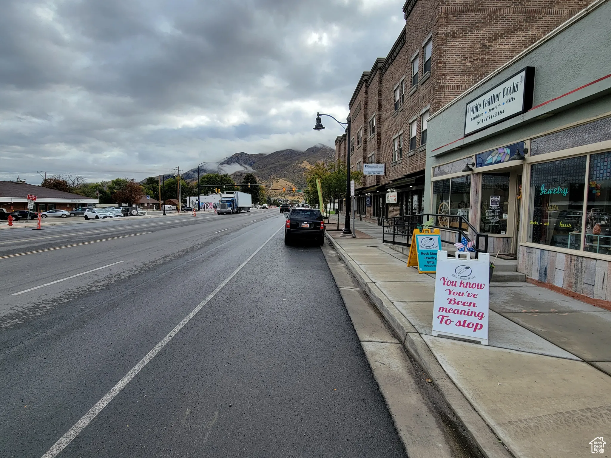 View of asphalt street with a mountain view, curbs, sidewalks, and street lights