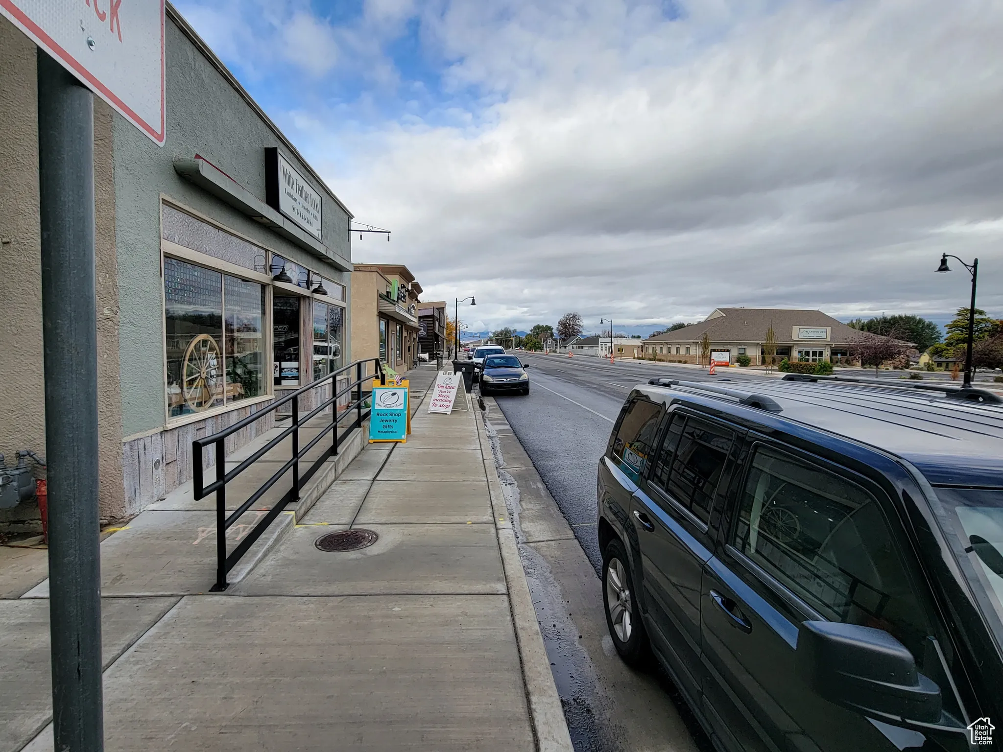 View of asphalt road featuring street lights, sidewalks, curbs & access ramp