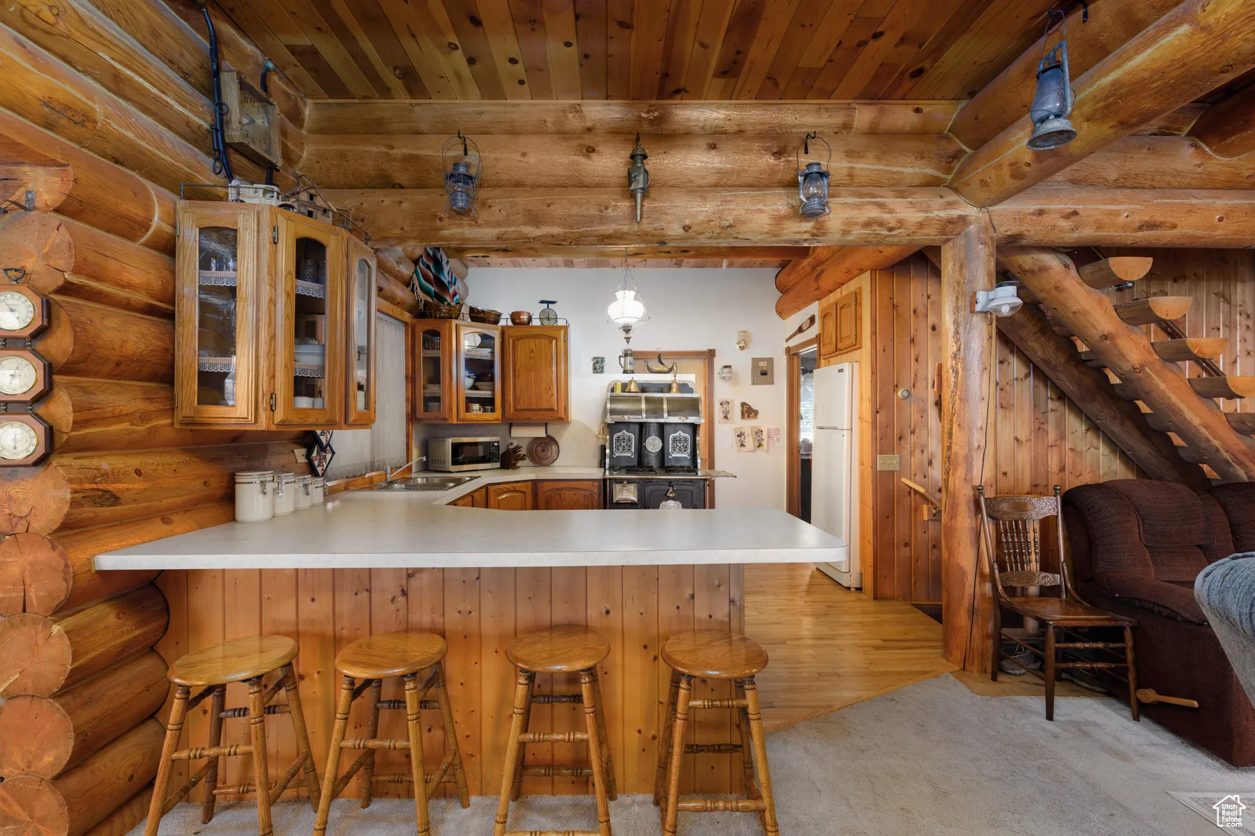 Kitchen with glass insert cabinets, log walls, light countertops, a peninsula, and brown cabinets