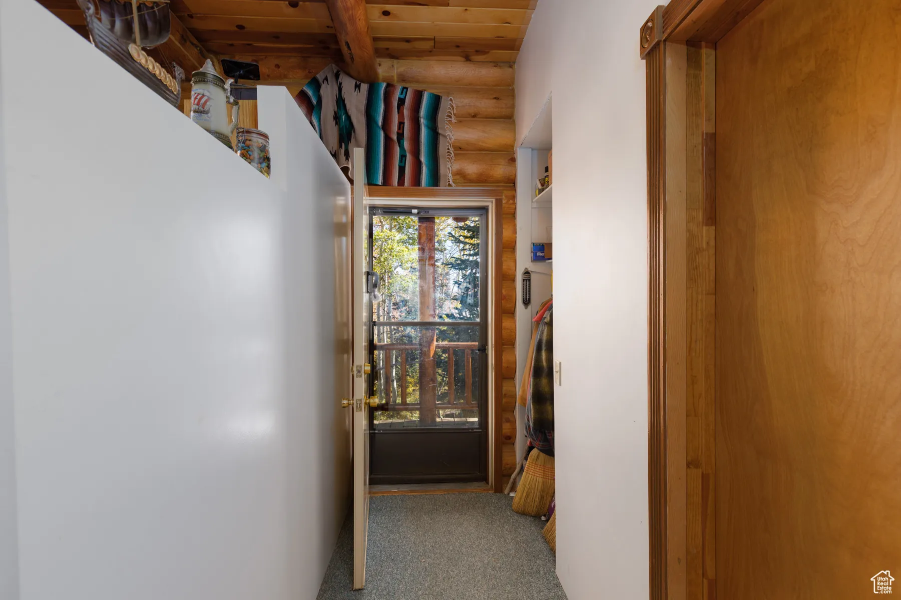 Hall featuring log walls, dark colored carpet, and a wooden ceiling with exposed beams