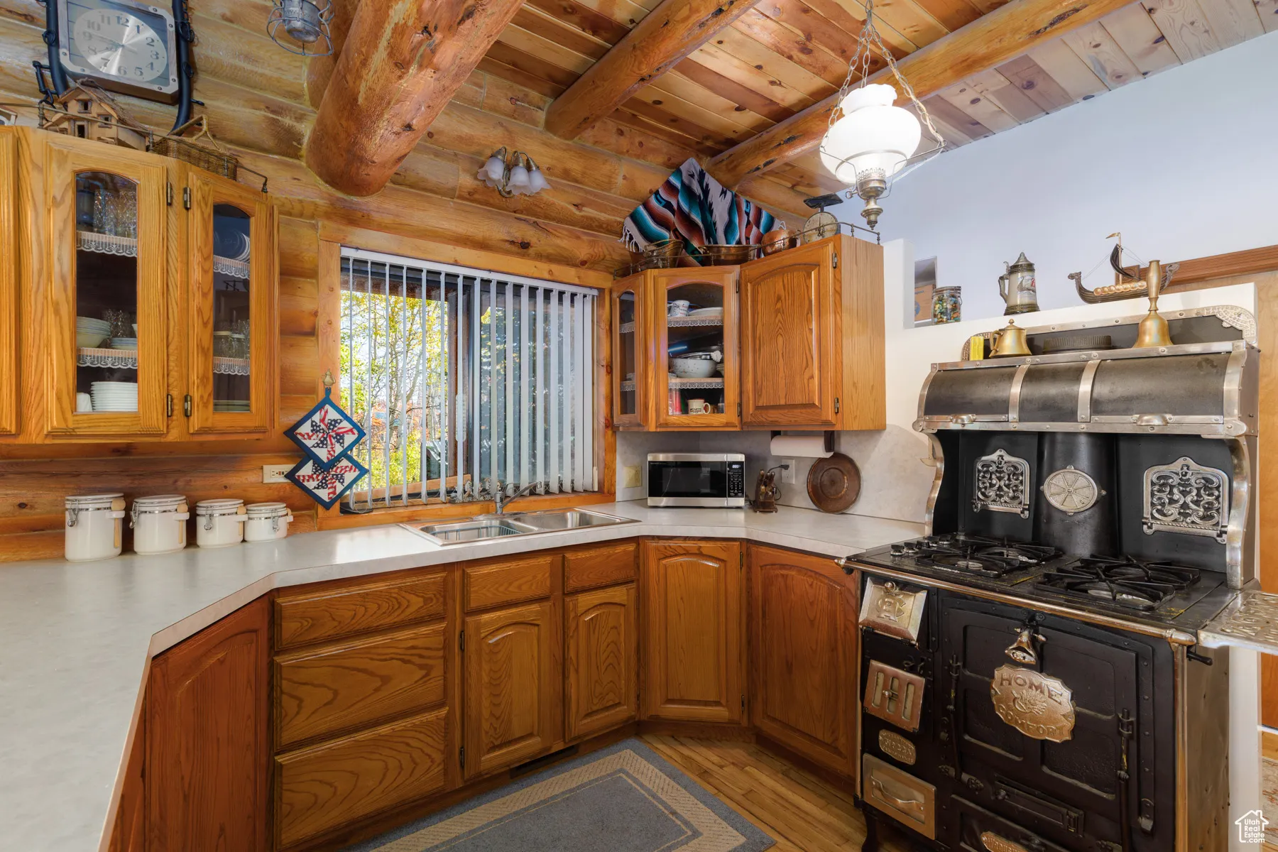 Kitchen featuring glass insert cabinets, light wood-style flooring, brown cabinets, light countertops, and hanging light fixtures
