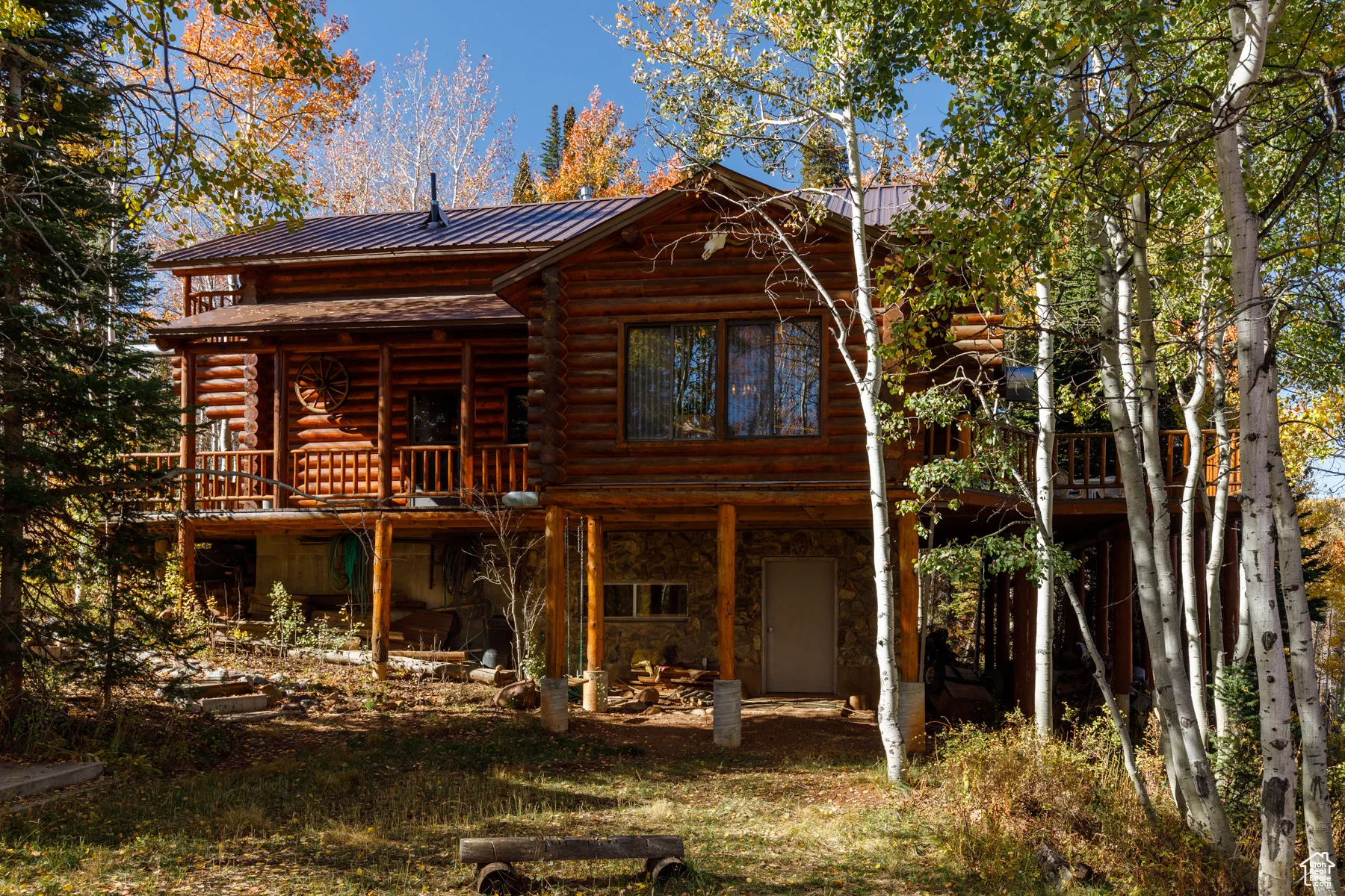 Rear view of house featuring log siding, a metal roof, and stone siding