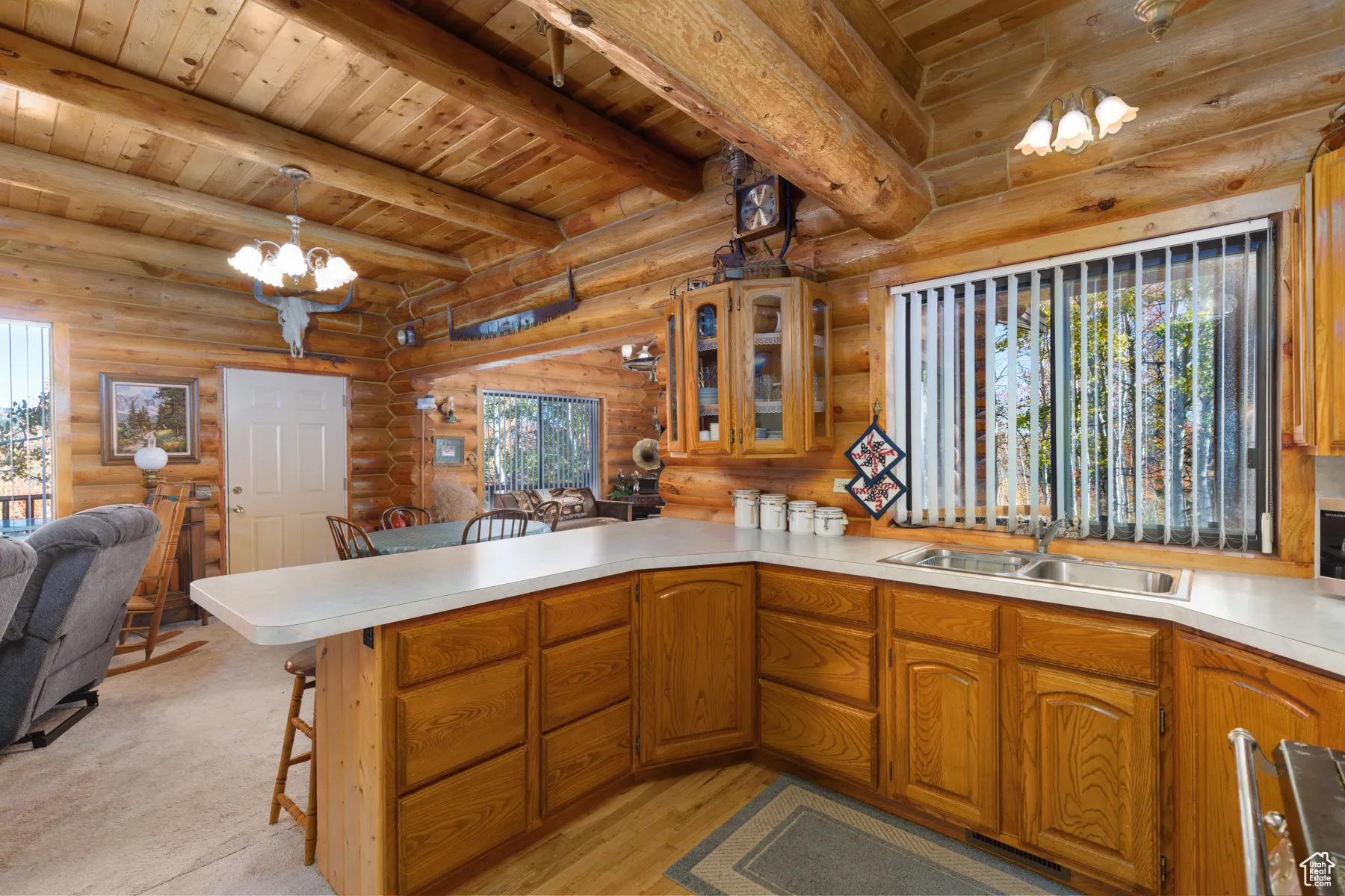 Kitchen featuring open floor plan, a kitchen breakfast bar, glass insert cabinets, a wooden ceiling with exposed beams, and a chandelier
