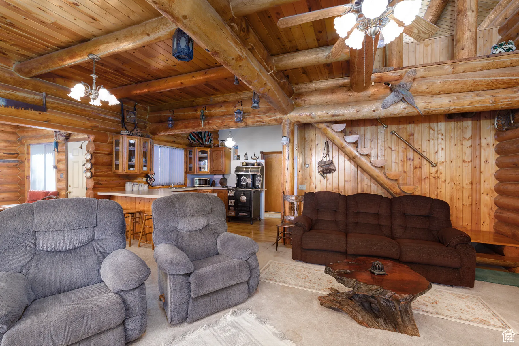 Living area with rustic walls, stairs, a wood ceiling with exposed beams, ceiling fan, and a chandelier