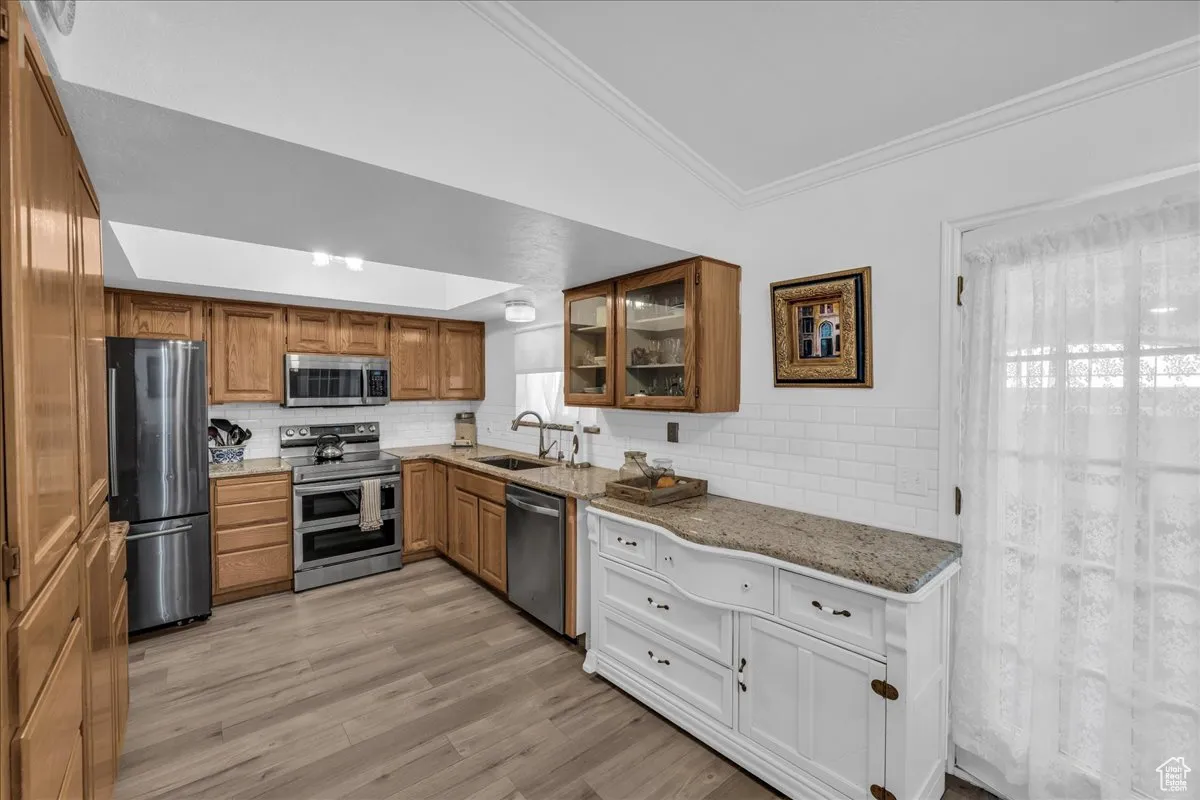 Kitchen with appliances with stainless steel finishes, ornamental molding, decorative backsplash, light stone countertops, and light wood-type flooring