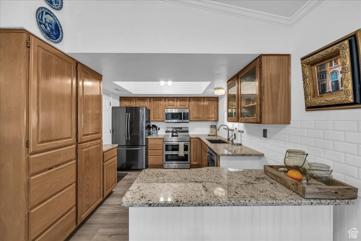 Kitchen with brown cabinets, glass insert cabinets, stainless steel appliances, light stone countertops, and ornamental molding