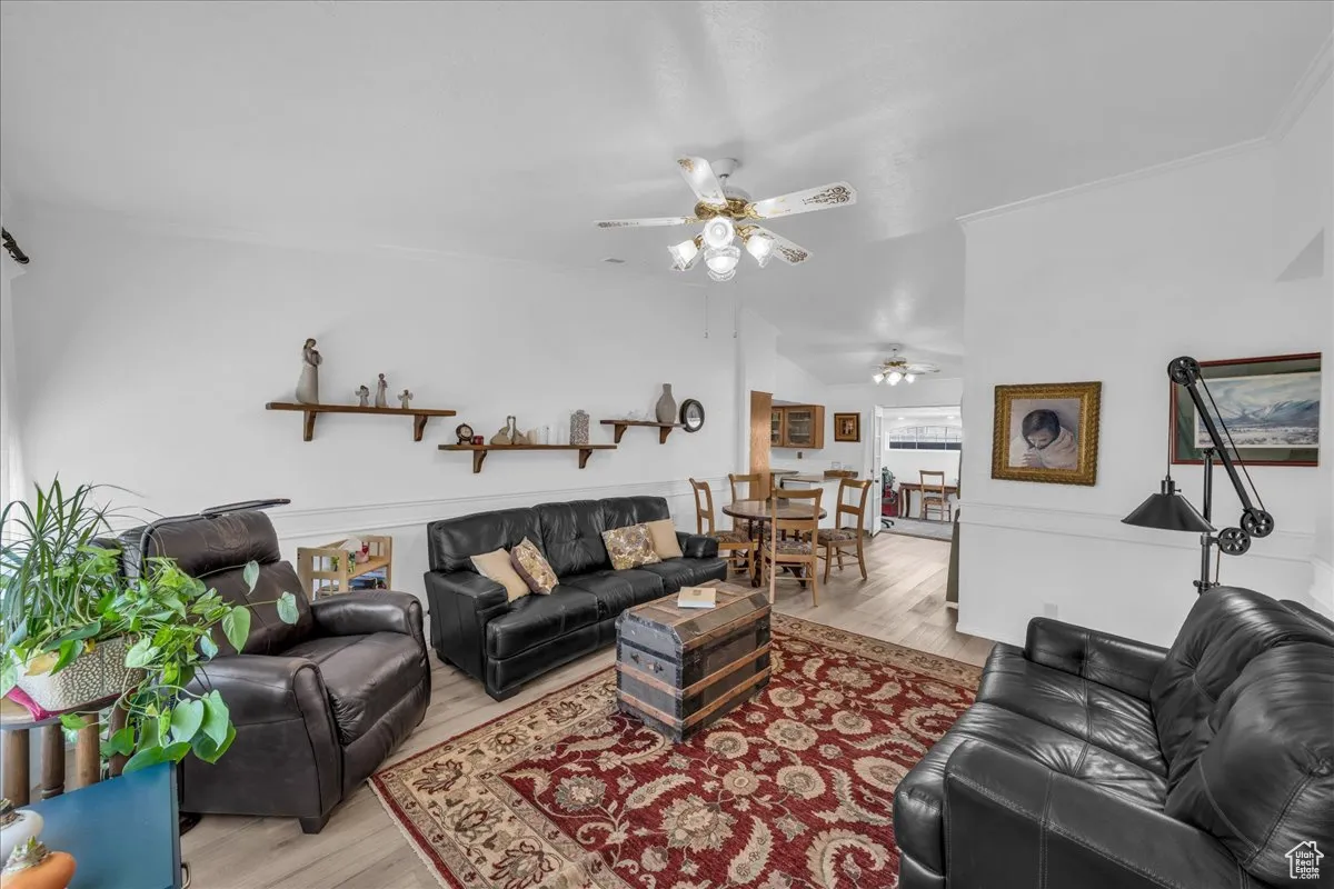 Living room featuring wood finished floors, a ceiling fan, vaulted ceiling, and ornamental molding
