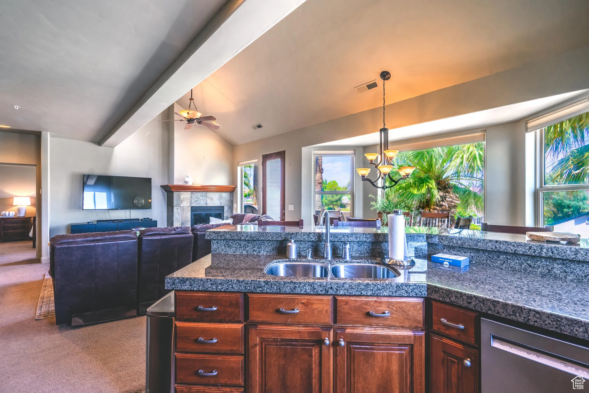 Kitchen featuring a tiled fireplace, stainless steel dishwasher, vaulted ceiling, dark colored carpet, and a chandelier