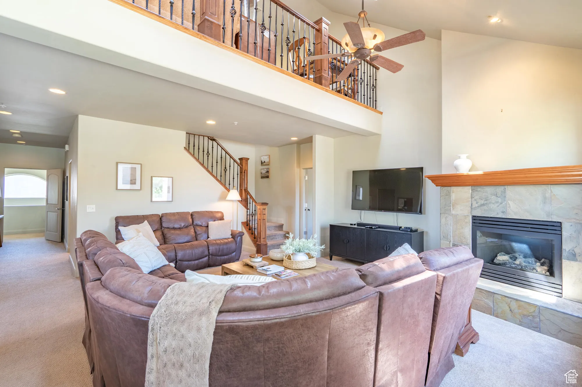 Living room featuring a towering ceiling, recessed lighting, a tile fireplace, carpet floors, and stairs