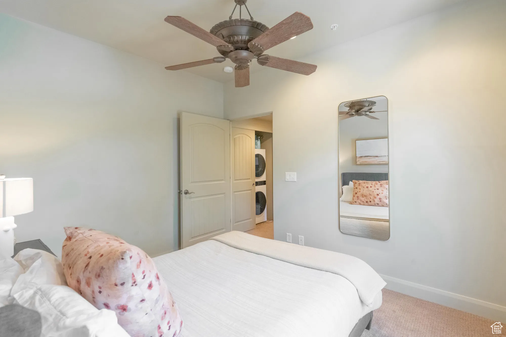 Carpeted bedroom featuring estacked washer and dryer and a ceiling fan
