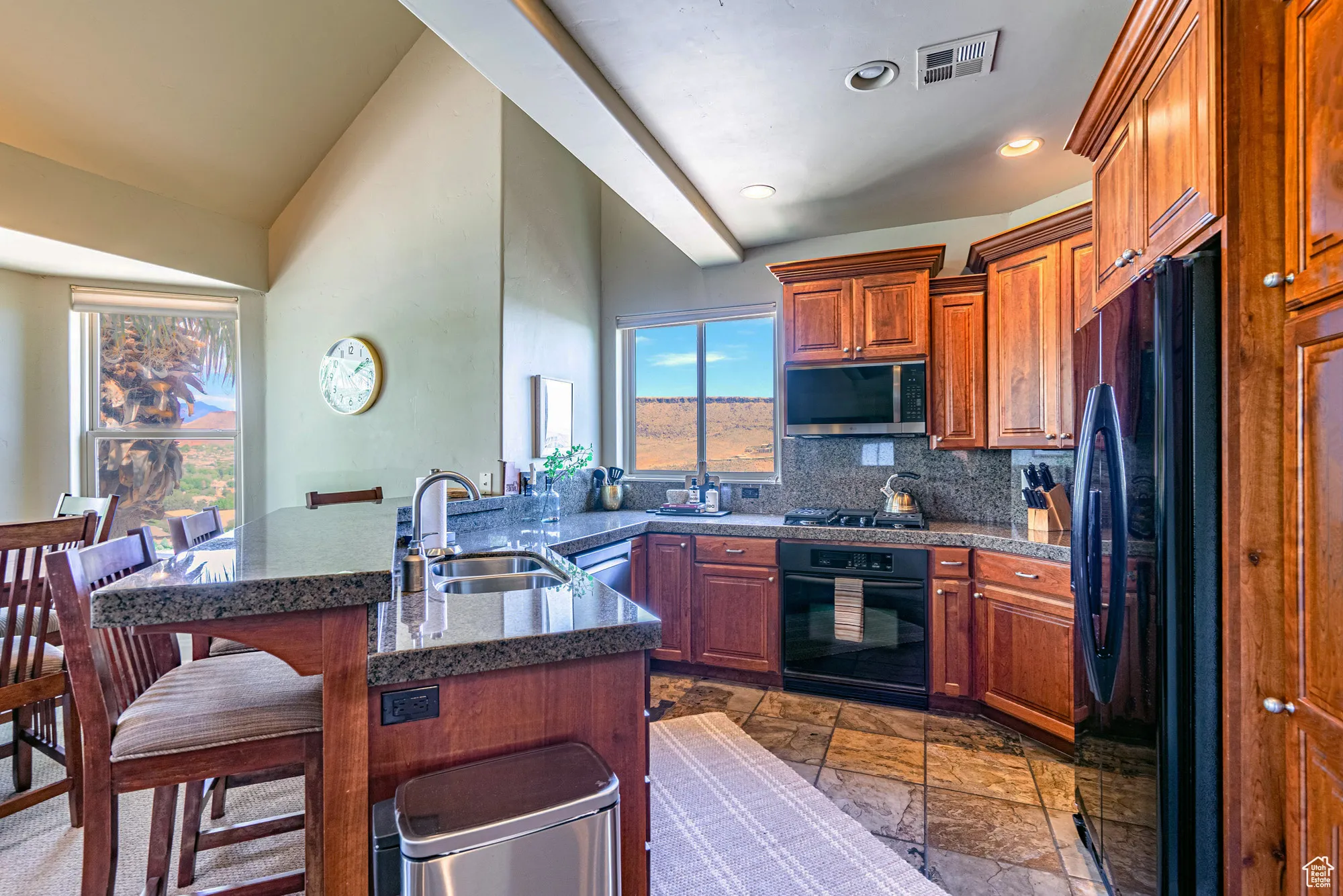 Kitchen featuring a breakfast bar area, brown cabinetry, black appliances, a peninsula, and backsplash