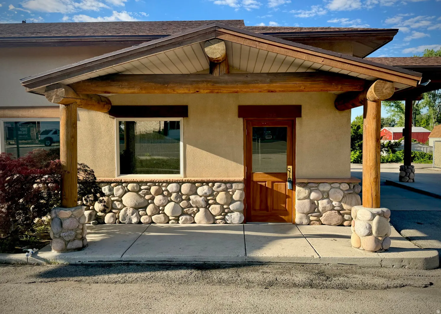 Rustic-inspired exterior featuring a wood-finish door with transom window, stone veneer siding, and natural log columns supporting a pitched roofline