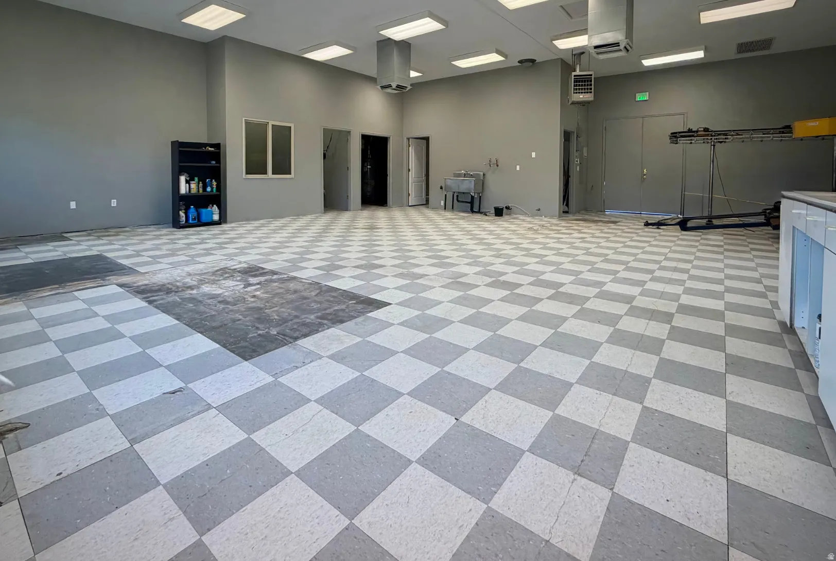 Expansive interior space featuring checkerboard-patterned flooring, multiple access points, and overhead fluorescent lighting