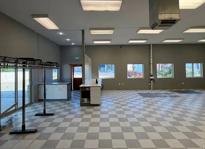 Spacious commercial interior featuring checkerboard flooring, multiple windows providing natural light, and abundant overhead lighting