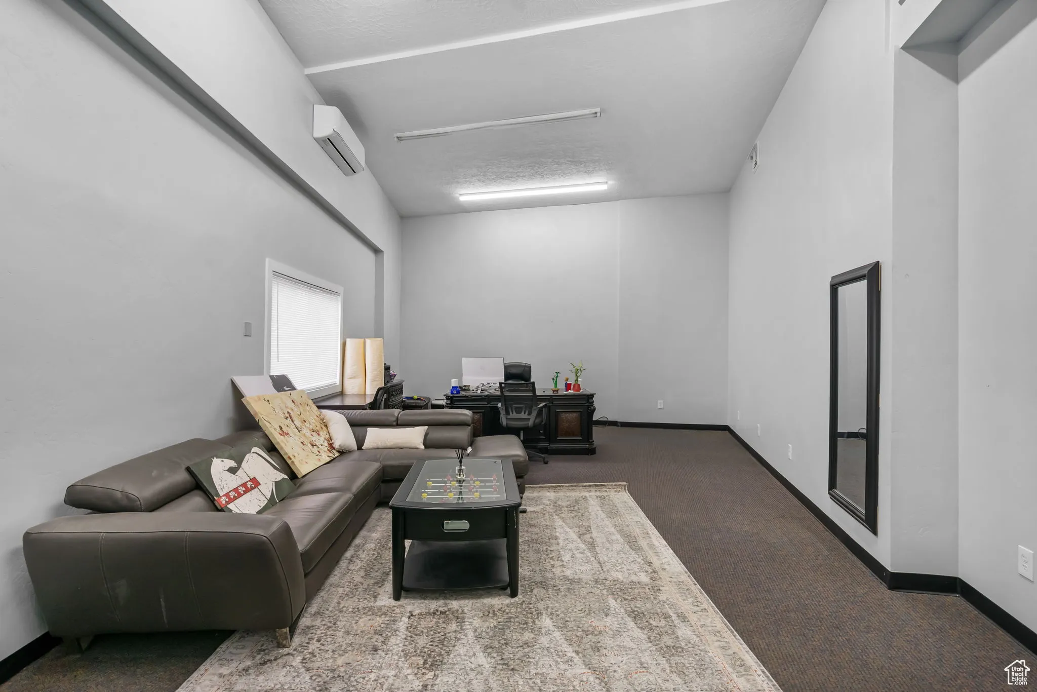 Living room with carpet floors, a wall mounted air conditioner, and a desk