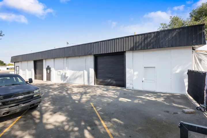 White exterior building featuring a black corrugated metal facade, multiple roll-up doors, and paved parking