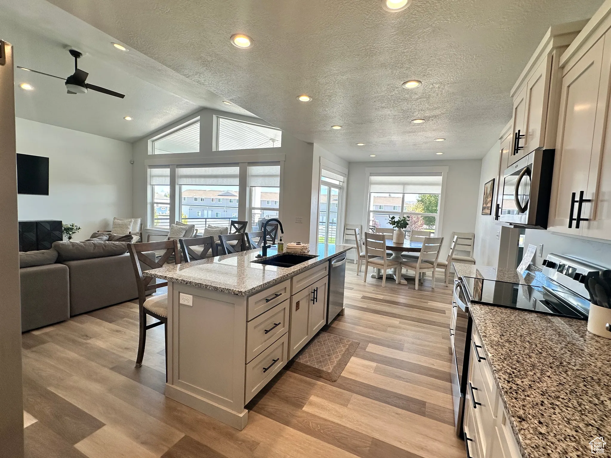 Kitchen featuring a kitchen bar, an island with sink, stainless steel appliances, light stone counters, and a textured ceiling