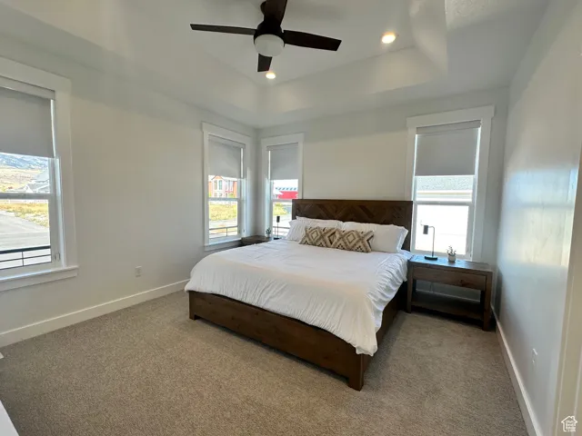 Carpeted bedroom with a raised ceiling, ceiling fan, and recessed lighting