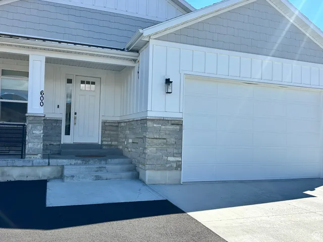 Doorway to property with board and batten siding, covered porch, stone siding, and driveway