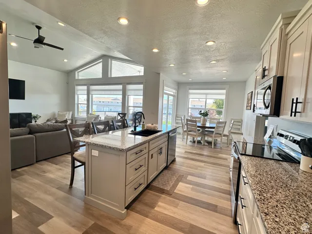 Kitchen featuring a kitchen bar, an island with sink, stainless steel appliances, light stone counters, and a textured ceiling
