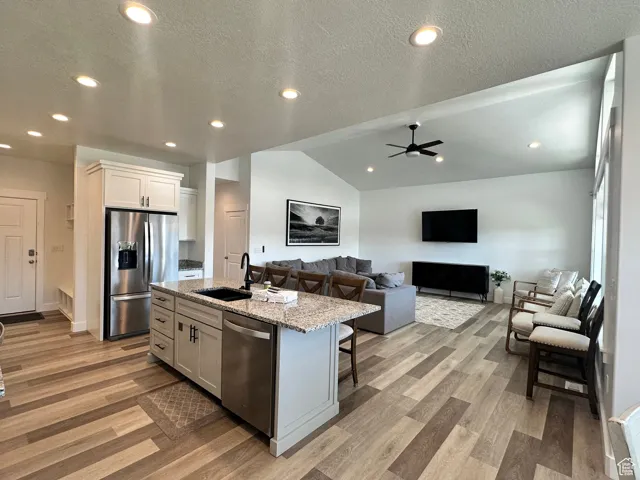 Kitchen featuring a textured ceiling, recessed lighting, light stone countertops, lofted ceiling, and appliances with stainless steel finishes