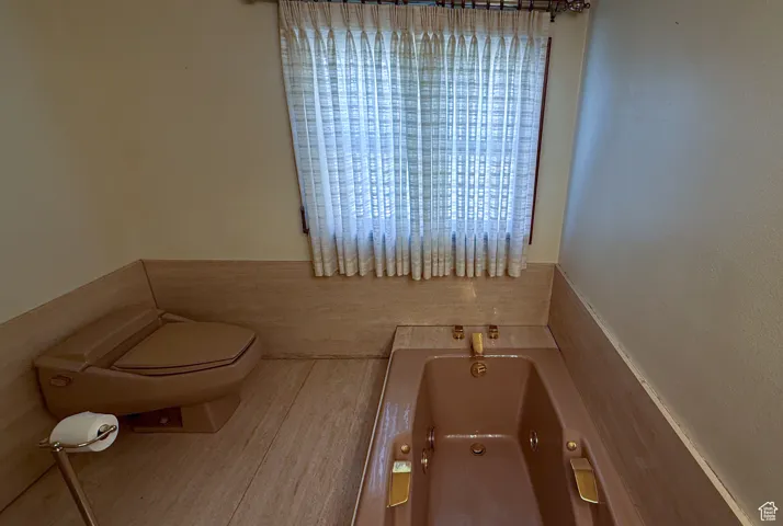 Bathroom featuring a whirlpool tub, wood finished floors, wainscoting, and tile walls