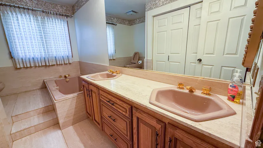 Full bathroom featuring light tile patterned floors, double vanity, and a garden tub