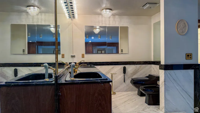 Bathroom featuring tile walls, a bidet, double vanity, and a chandelier