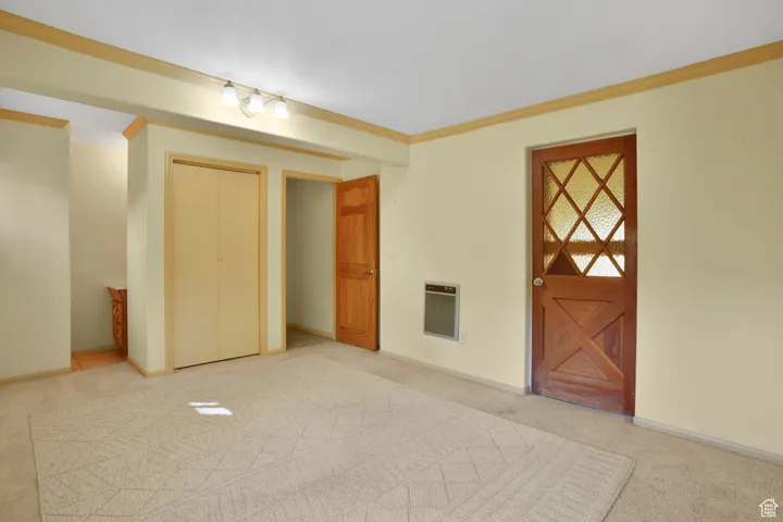 Unfurnished bedroom with ornamental molding, carpet floors, heating unit, and a closet