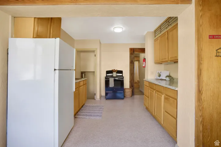 Kitchen with freestanding refrigerator, light countertops, black range with electric stovetop, and light brown cabinetry