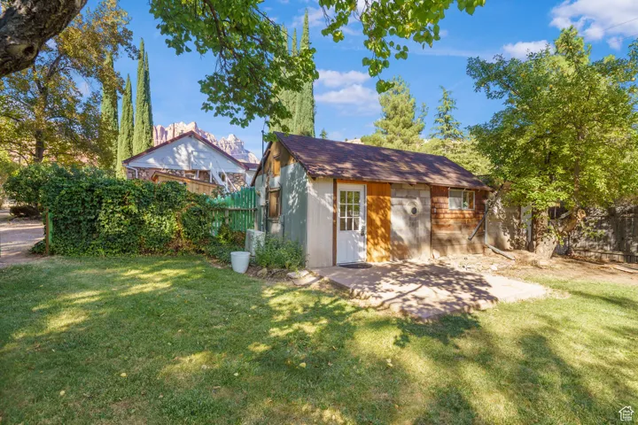 Rear view of property featuring an outbuilding, roof with shingles, and a patio