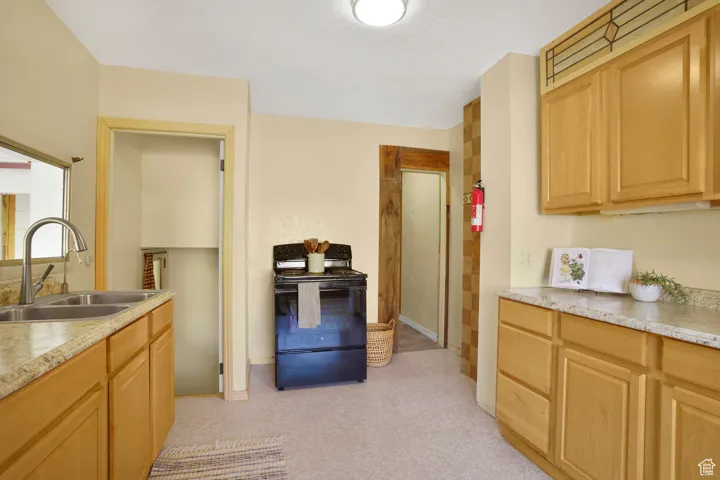 Kitchen with light countertops, black range with electric stovetop, light brown cabinetry, and light carpet