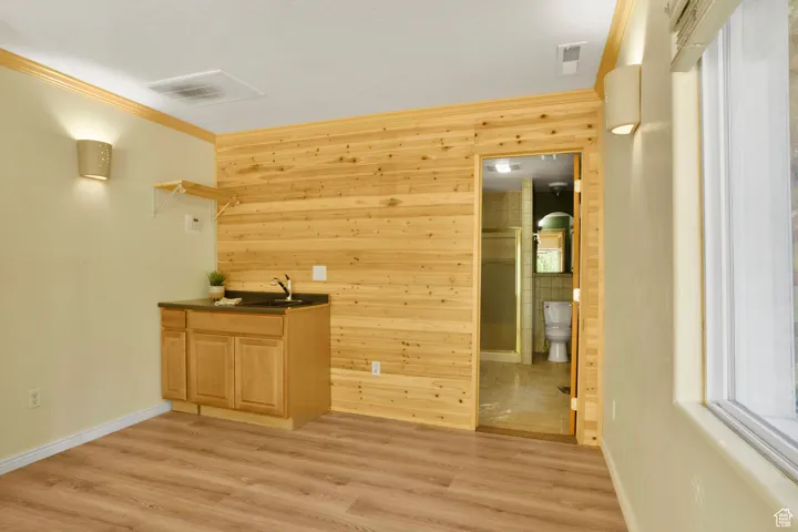 Bar area featuring crown molding, wooden walls, light wood-style floors, dark countertops, and light brown cabinets