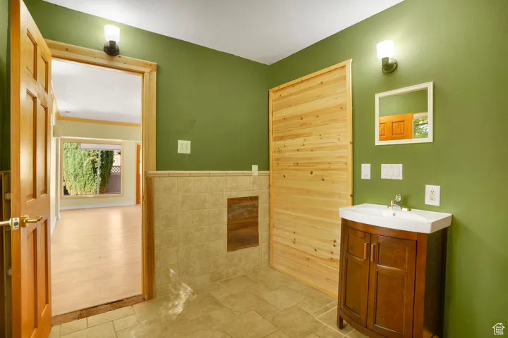Bathroom featuring stone tile flooring, vanity, tile walls, and a wainscoted wall
