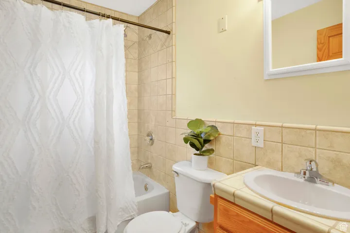 Full bathroom featuring shower / bath combo, vanity, and tile walls