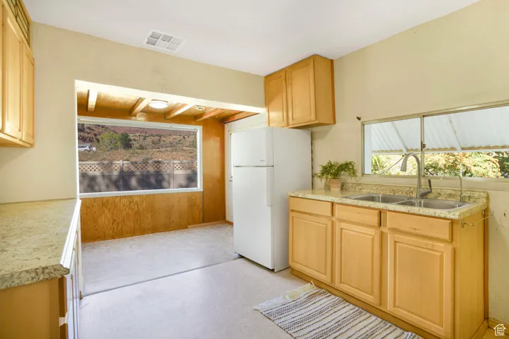 Kitchen with freestanding refrigerator, light brown cabinets, beamed ceiling, and wooden walls