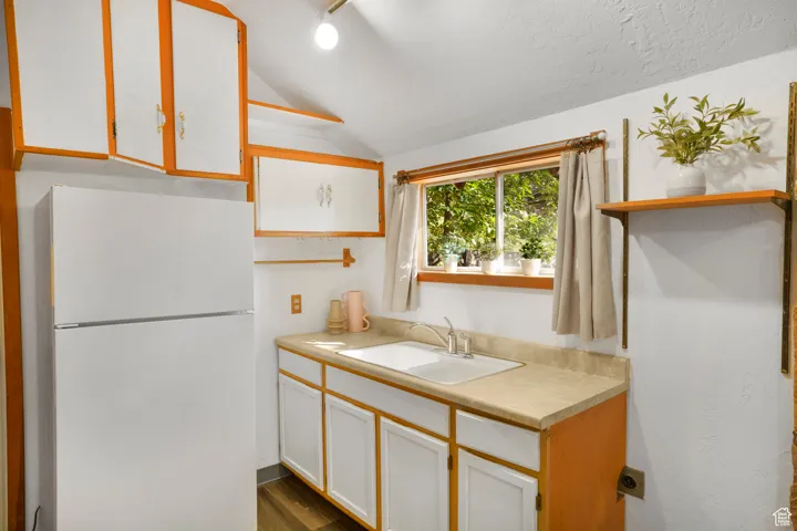 Kitchen featuring open shelves, white cabinetry, freestanding refrigerator, and lofted ceiling