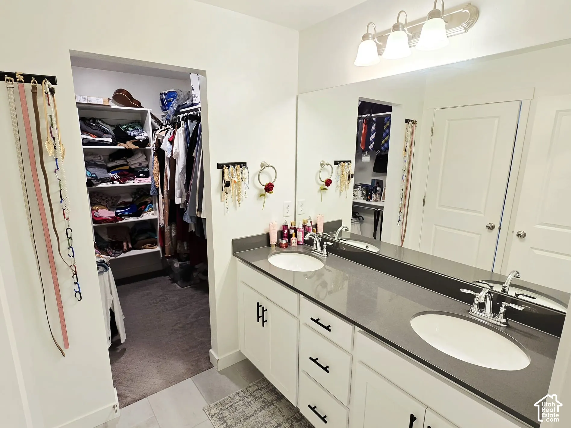 Full bath with double vanity, light colored carpet, a spacious closet, and light tile patterned floors