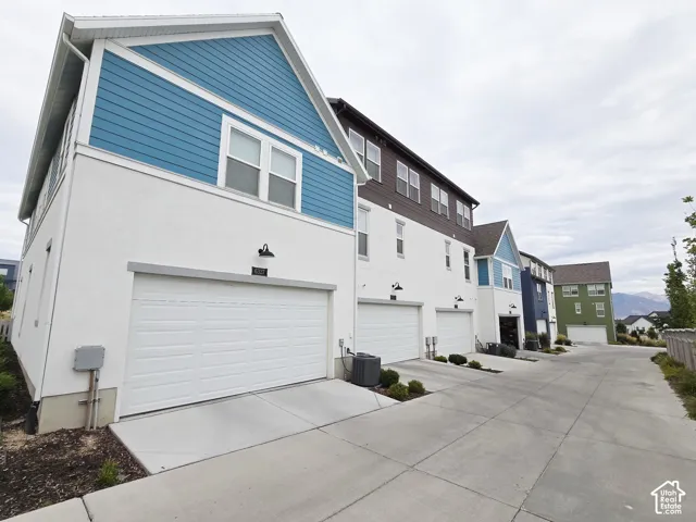Back of house featuring concrete driveway, a residential view, an attached garage, and stucco siding