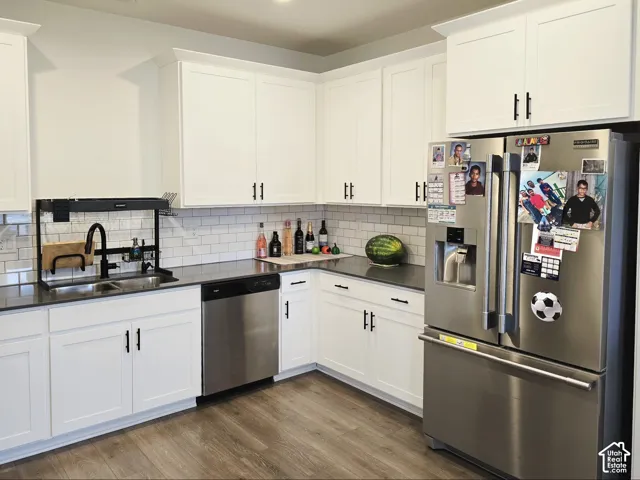 Kitchen with appliances with stainless steel finishes, white cabinetry, dark wood-style flooring, and decorative backsplash
