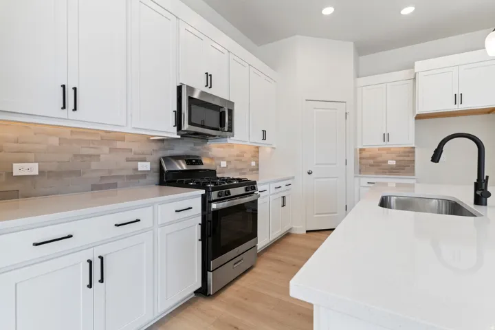 Kitchen with stainless steel appliances, white cabinetry, light stone countertops, tasteful backsplash, and recessed lighting