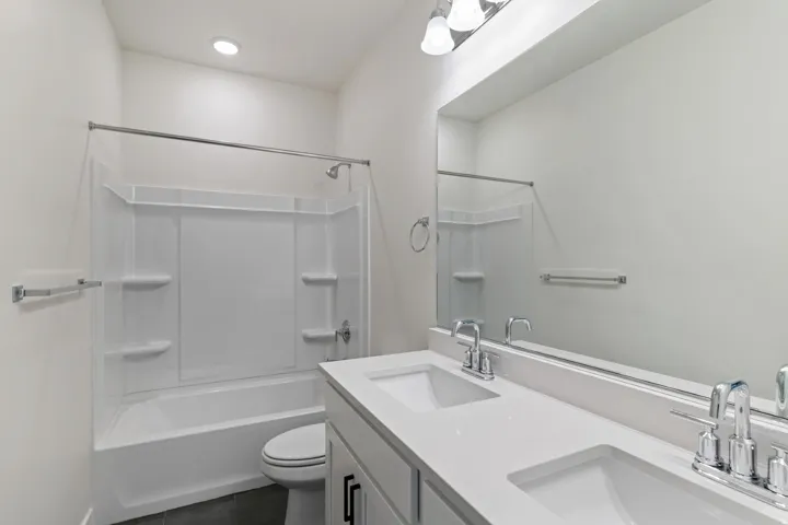 Bathroom featuring shower / tub combination, double vanity, and dark tile patterned flooring
