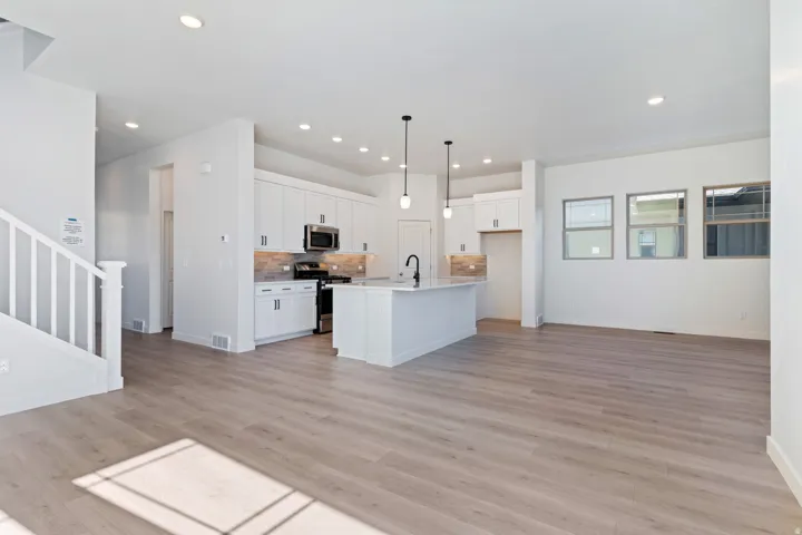 Kitchen featuring tasteful backsplash, open floor plan, white cabinetry, an island with sink, and hanging light fixtures