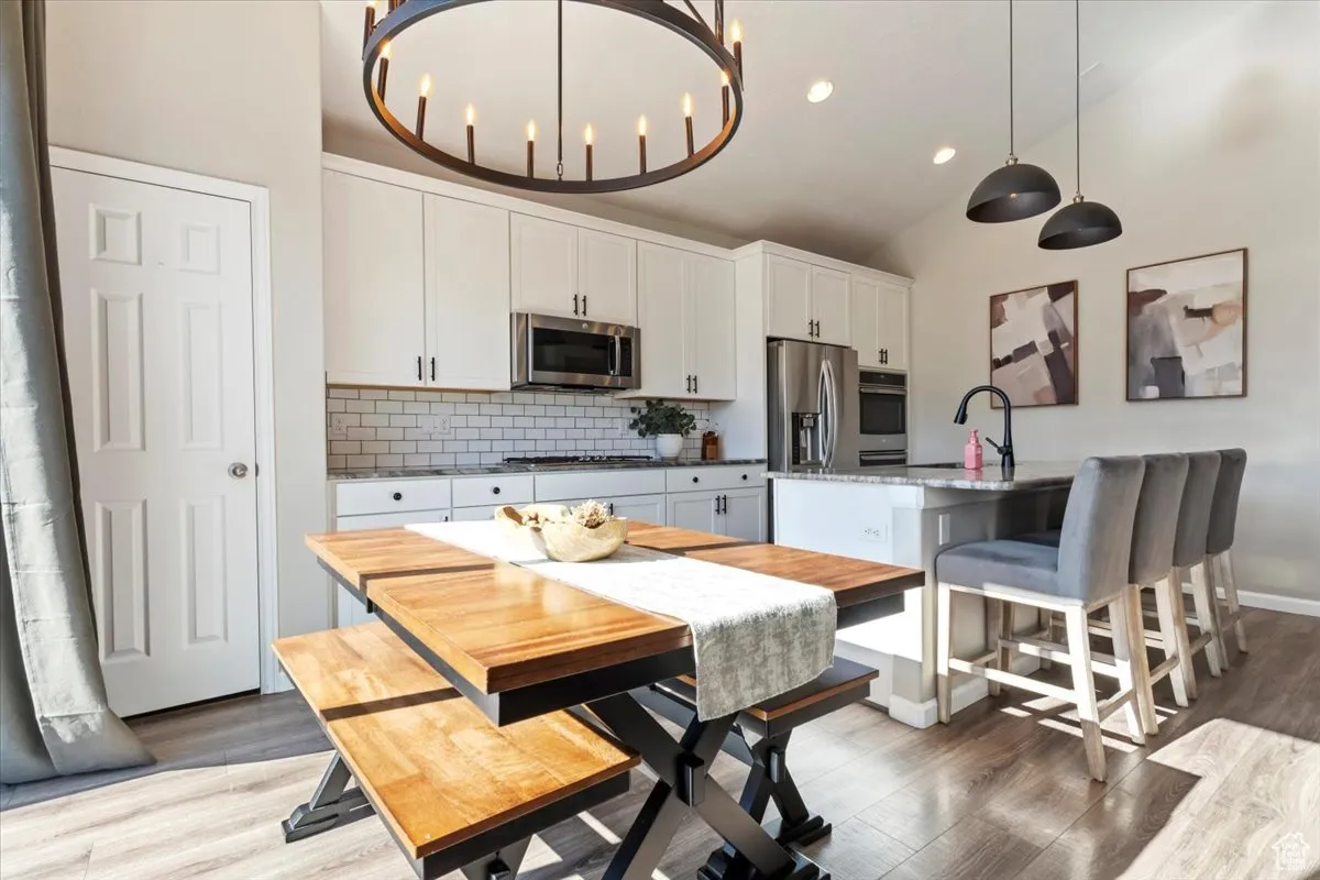 Kitchen with tasteful backsplash, white cabinets, appliances with stainless steel finishes, a kitchen breakfast bar, and an island with sink