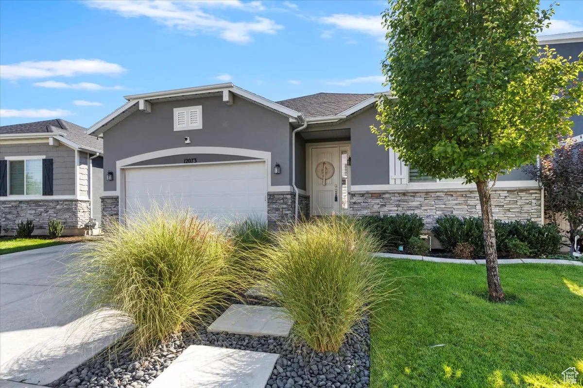 View of front of home featuring stone siding, stucco siding, a front lawn, and a garage