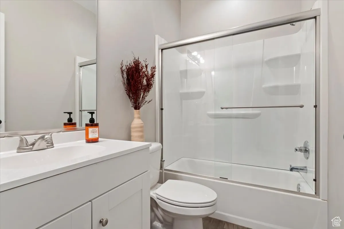 Bathroom with bath / shower combo with glass door, vanity, and wood finished floors