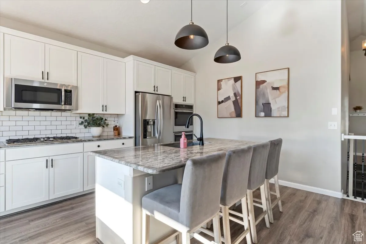 Kitchen with light stone countertops, stainless steel appliances, tasteful backsplash, light wood-style flooring, and a kitchen breakfast bar