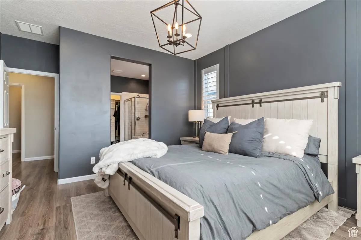 Bedroom with wood finished floors, a textured ceiling, a chandelier, and ensuite bath