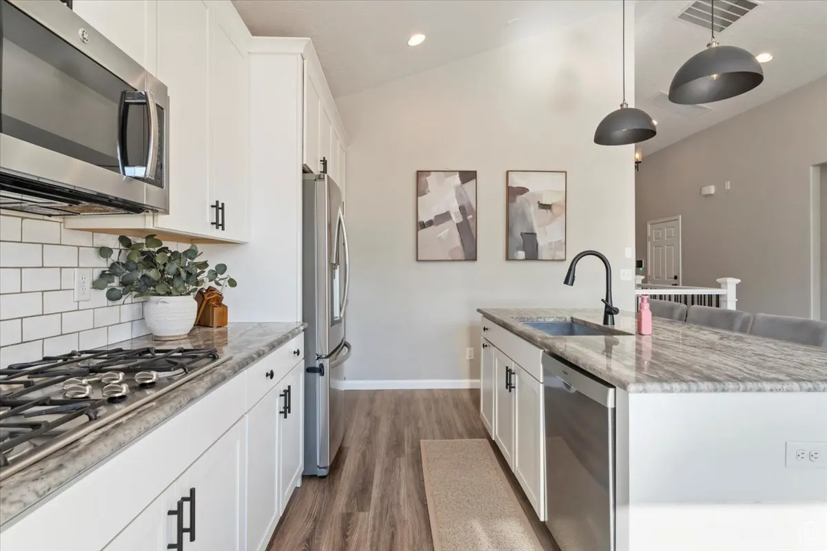 Kitchen with white cabinets, stainless steel appliances, vaulted ceiling, light stone countertops, and decorative light fixtures