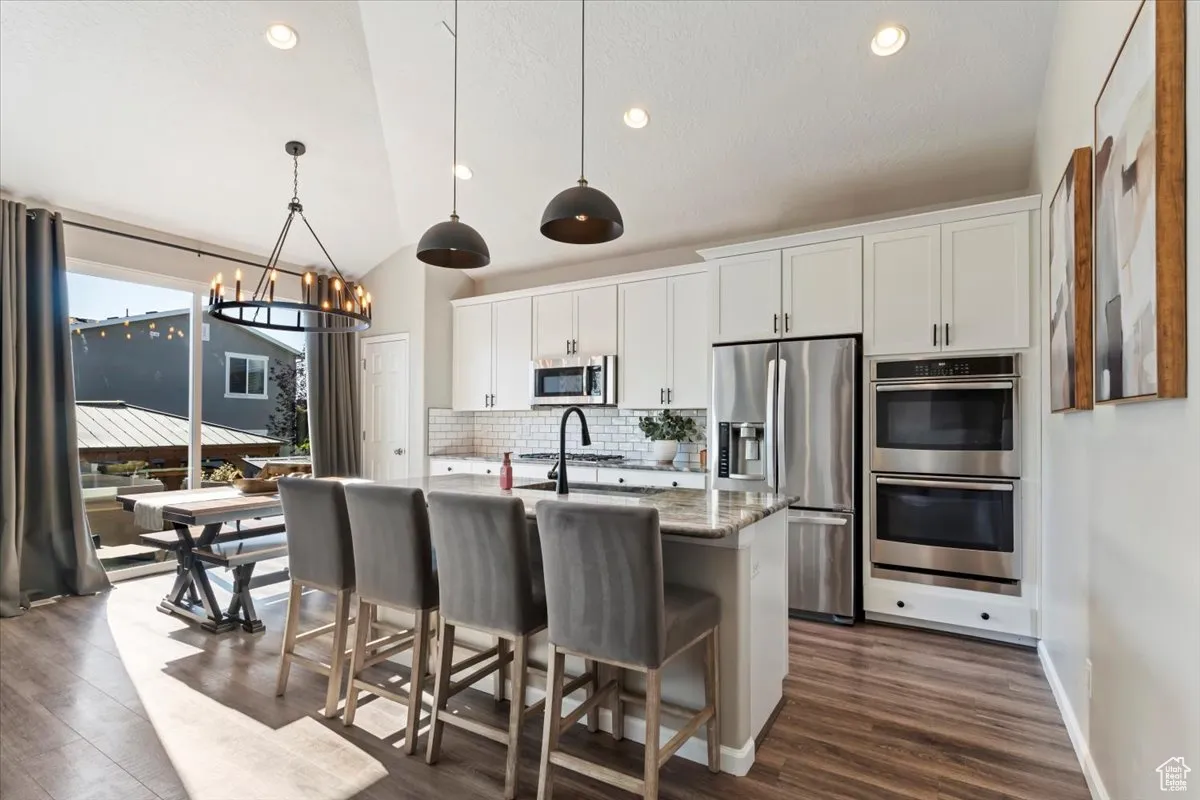 Kitchen with hanging light fixtures, stainless steel appliances, a breakfast bar area, white cabinets, and a chandelier